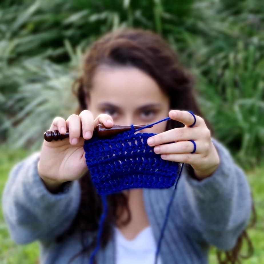 project in progress - girl holding a black crochet hook and blue yarn with text “Hey, There!”