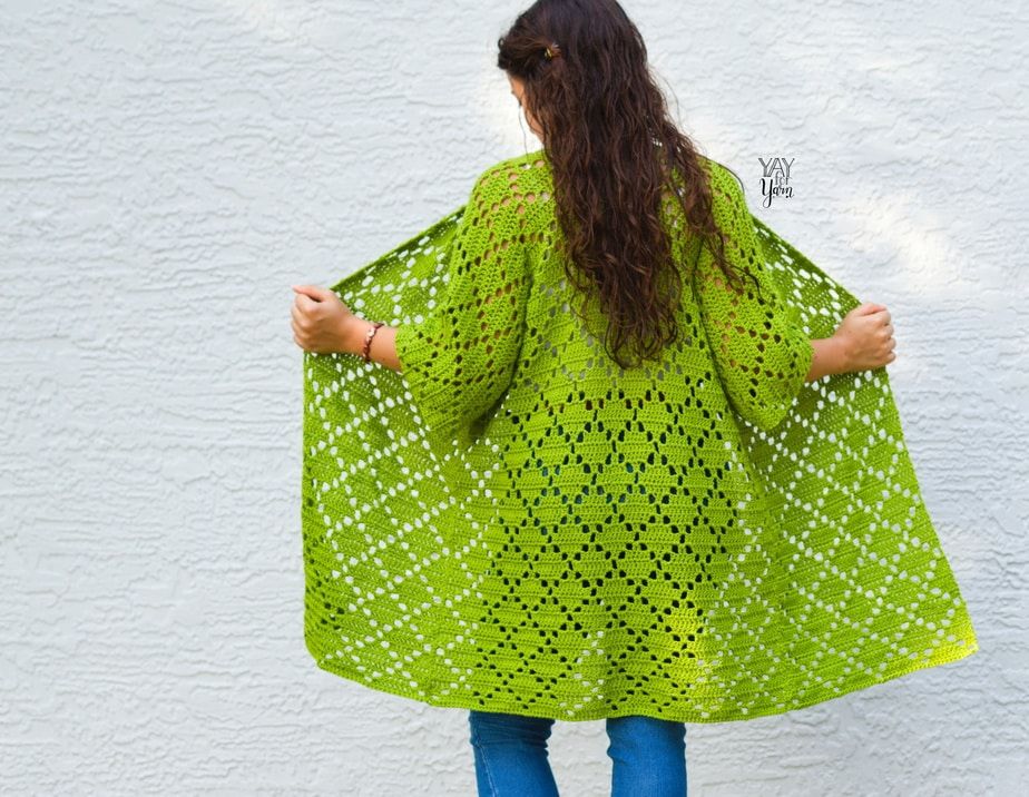 girl opening green crocheted cardigan to show the back