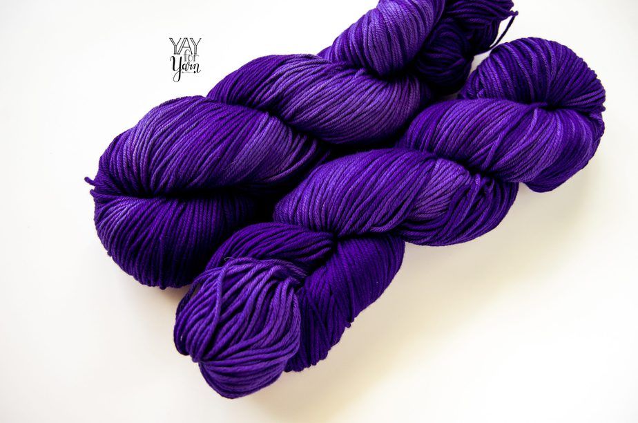 two skeins of purpleish navy blue hand dyed yarn on white background, shown at a diagonal angle