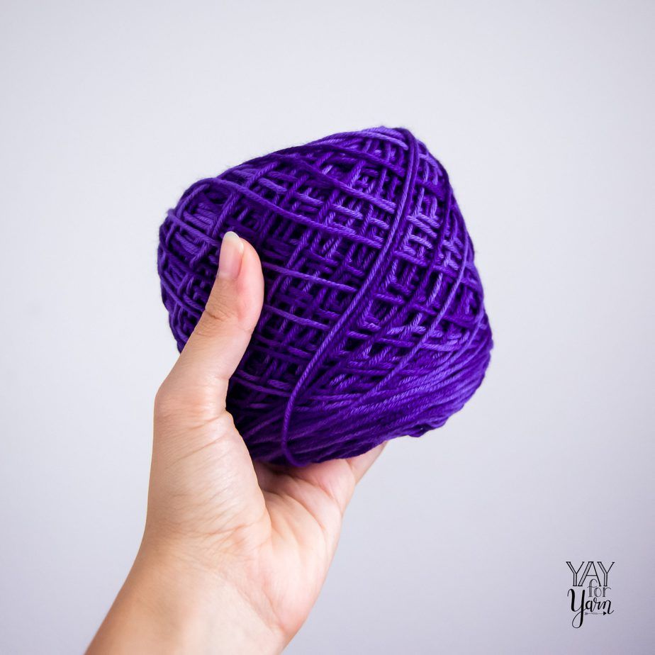 hand holding a center-pull cake of deep blue tonal yarn on white background