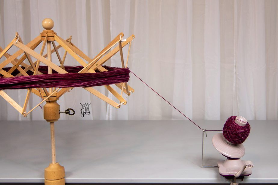 knitpicks birch yarn swift and ball winder on grey table, winding a deep purplish red yarn