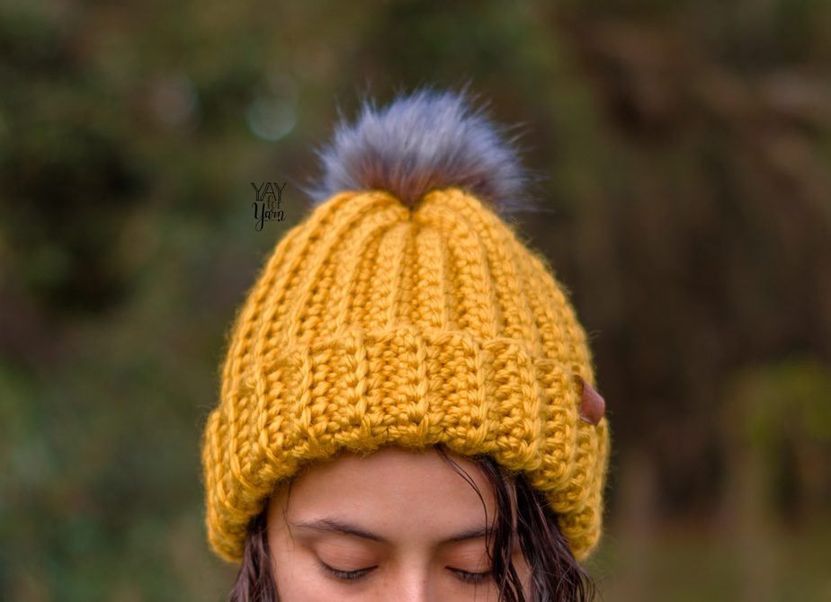 Close-up of a girl outdoors wearing yellow crochet ski hat with gray fur pom pom