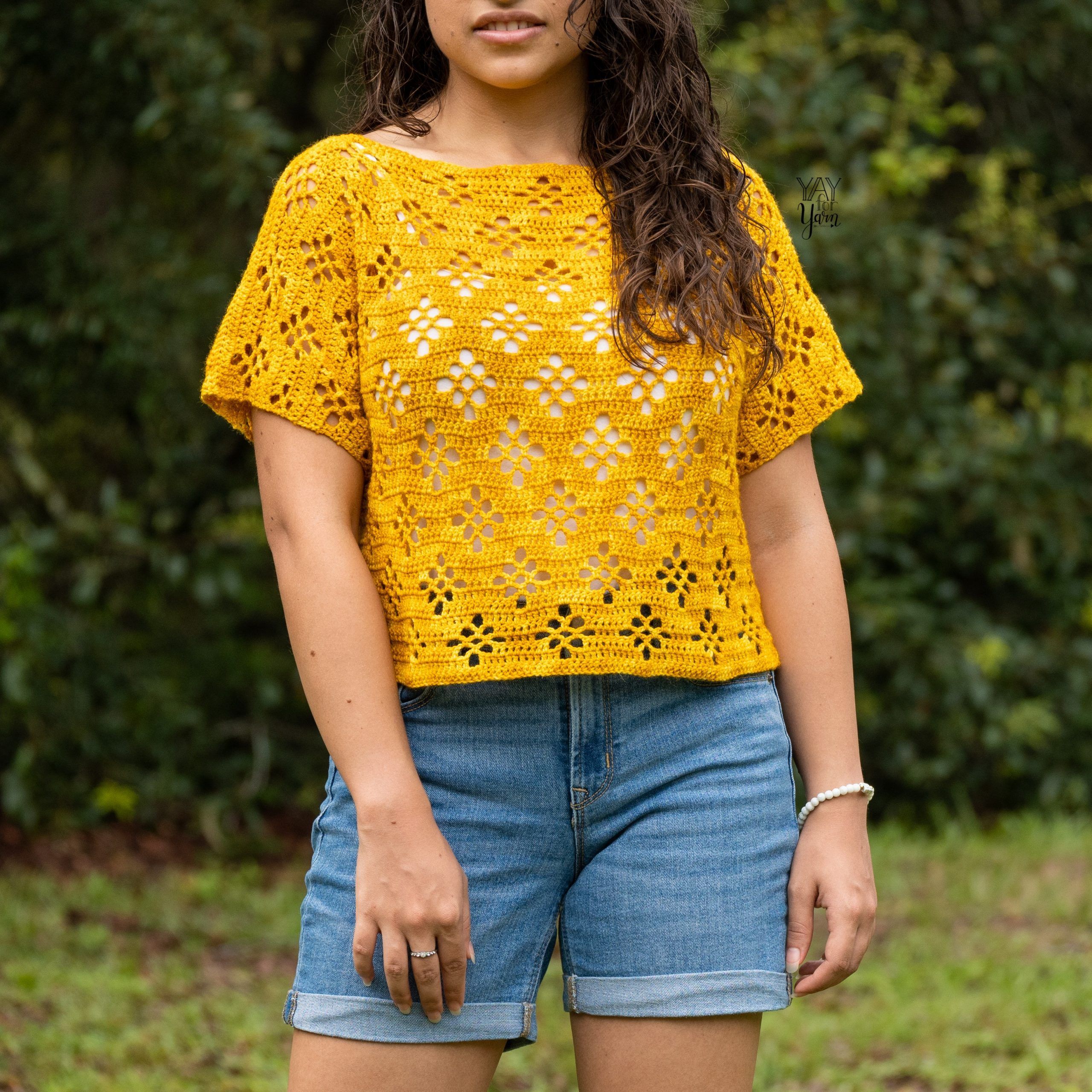 woman standing outdoors wearing bright yellow lace crochet tee with jean shorts